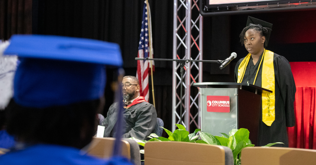 student standing on stage in cap and gown